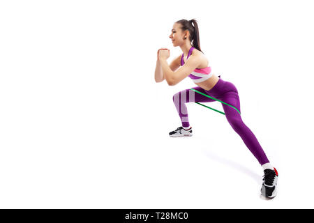 A young woman coach in a sporty pink short top and gym shows the correct squatting technique with sport fitness rubber bands; the position of a full s Stock Photo