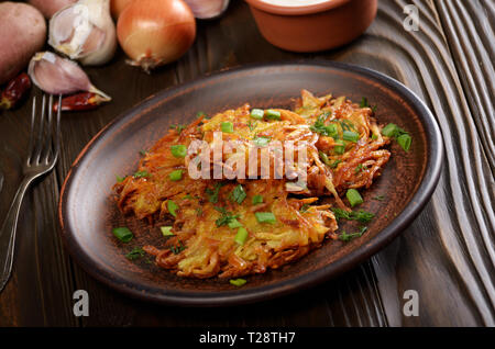 Fresh homemade tasty potato pancakes in clay dish with vegetables on wooden table Stock Photo