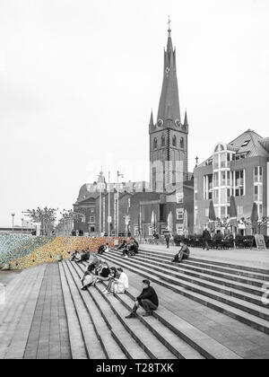 Düsseldorf, Germany, 23 March 2019. People sitting on steps in front of colorful Mosaic on the promenade on the bank of river Rhine. Stock Photo