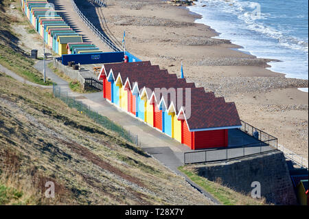 People walking past the Colourful beach huts, west cliff, Whitby, North Yorkshire Coast, England, UK, GB.