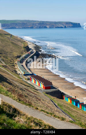 People walking past the Colourful beach huts, west cliff, Whitby, North Yorkshire Coast, England, UK, GB.