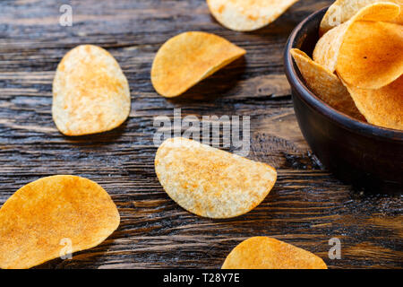 Crispy potato chips in a clay plate on old kitchen table Stock Photo