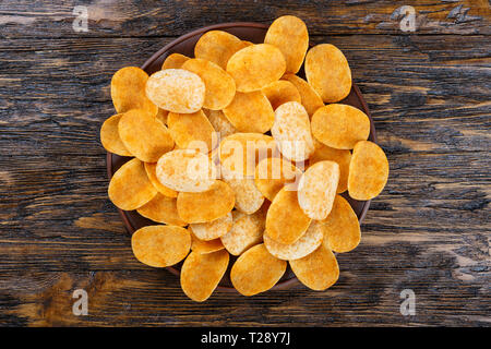 Crispy potato chips in a clay plate on old kitchen table Stock Photo