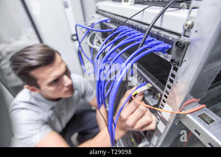 Young man working in network server room with fiber optic hub for digital communications and internet Stock Photo
