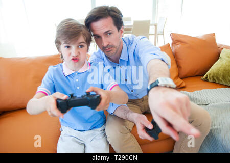 Father and son sitting on sofa in lounge playing video game Stock Photo