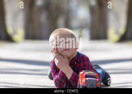 Cute little child, blonde toddler boy playing outdoors lying at street Stock Photo