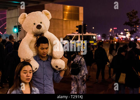 Man carrying huge teddy bear on shoulders, and street filled with people, during Chinese New Year celebrations, Kowloon, Hong Kong Stock Photo