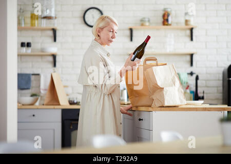 Mature lady unpacking paper bags in kitchen Stock Photo