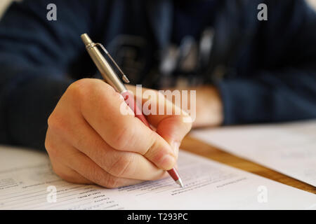 Man hand with pen. Close up of the hand of a man fill in a contract. Selective focus on hand. Blurred agreement content Stock Photo