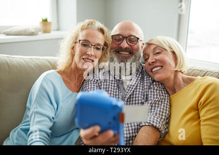 Excited mature friends taking selfie on instant camera Stock Photo