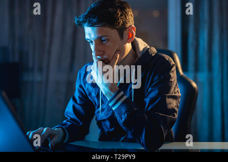 A young man working on a laptop at night. The designer or system administrator stayed late at work. Stock Photo