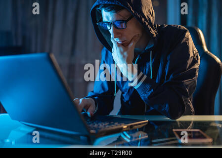 Cybercriminal hacker in the hood typing program code while stealing access databases with passwords. The concept of cyber security Stock Photo