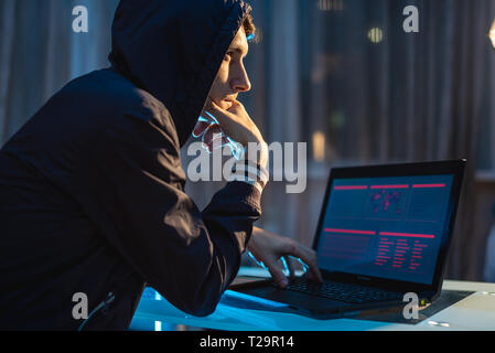 A male hacker in the hood thinking about the problem of hacking and stealing access databases with passwords. The concept of cybersecurity Stock Photo