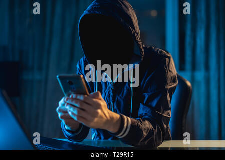 Anonymous hacker programmer uses a laptop to hack the system in the dark. Creation and infection of malicious virus. The concept of cybercrime and hac Stock Photo
