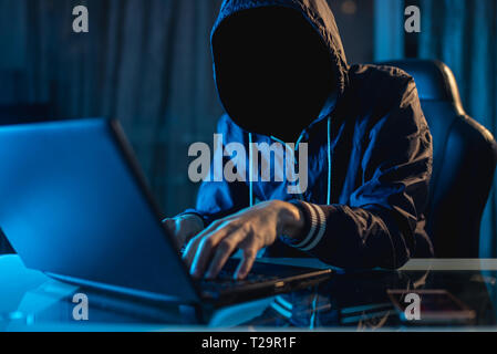 Anonymous hacker programmer uses a laptop to hack the system in the dark. Creation and infection of malicious virus. The concept of cybercrime and hac Stock Photo