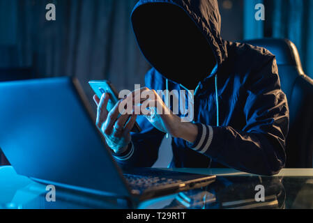 Anonymous hacker programmer uses a laptop to hack the system in the dark. Creation and infection of malicious virus. The concept of cybercrime and hac Stock Photo