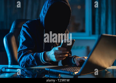 Anonymous hacker programmer uses a laptop to hack the system in the dark. Creation and infection of malicious virus. The concept of cybercrime and hac Stock Photo