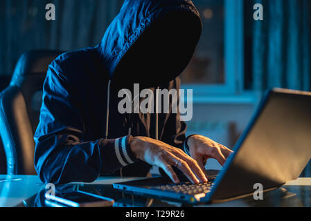 Anonymous hacker programmer uses a laptop to hack the system in the dark. Creation and infection of malicious virus. The concept of cybercrime and hac Stock Photo