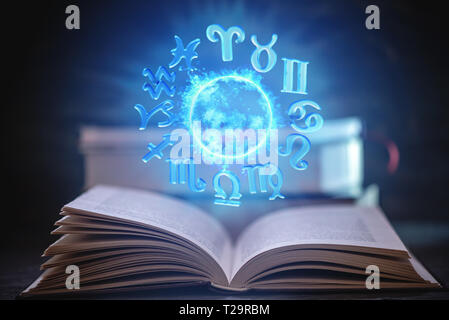 Open book on astrology on a dark background. The glowing magical globe with signs of the zodiac in the blue light. Prediction and magic Stock Photo
