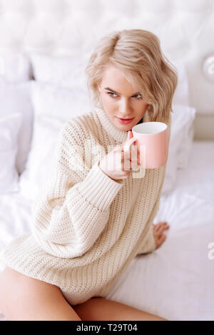 Young woman wearing beige sweater holding pink cup of tea Stock Photo