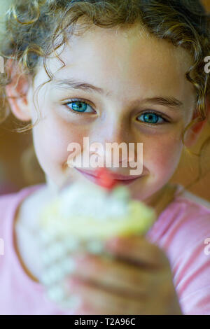 Girl holding up a cupcake and smiling Stock Photo