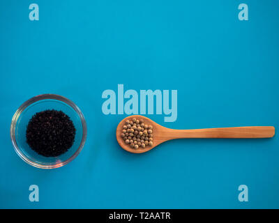 Crystal bowl with common marine salt and a wooden spoon with white peppercorns on a blue background Stock Photo