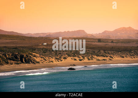 Blue ocean waves rolling onto golden sandy beach under a late afternoon yellow sky. Stock Photo