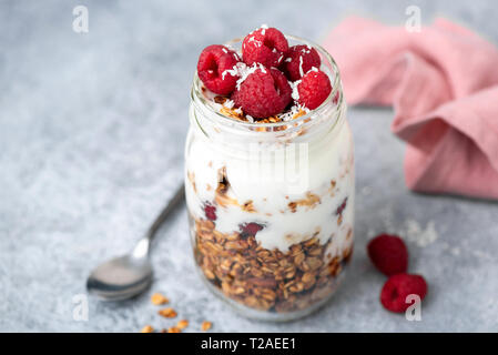 Granola, yogurt and berries in jar on concrete table background. Closeup view, selective focus. Tasty breakfast parfait with greek yogurt and crunchy  Stock Photo