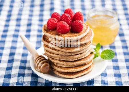 Whole wheat pancakes with raspberries, honey on blue checkered table textile Stock Photo