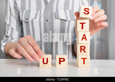 Hand of female putting wood cube block with words START UP on table. Start up concept Stock Photo