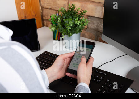 Close-up of female hands using modern smart phone while working at office with computer, businesswoman typing text message on her cellphone Stock Photo