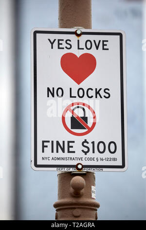 No Padlock fine sign warning romantic couple against fixing locks to the Brooklyn Bridge  Manhattan, New York at night Stock Photo