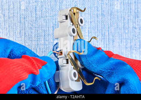 Worker in protective gloves is inserting wires in electrical outlet, close-up. Stock Photo
