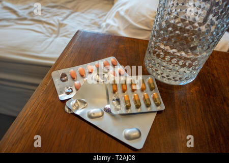 3 packets of Prescription drugs and a glass of water on a bedside table