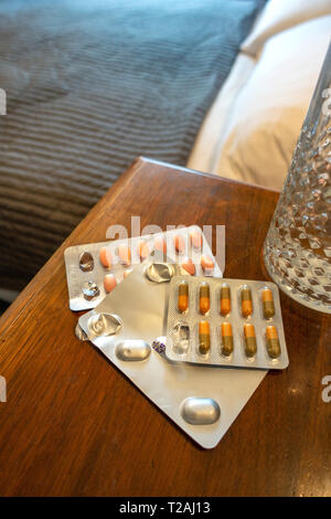 3 packets of Prescription drugs and a glass of water on a bedside table