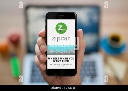 A man looks at his iPhone which displays the Zipcar logo (Editorial use only). Stock Photo