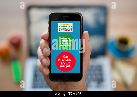 A man looks at his iPhone which displays the People’s Postcode Lottery logo (Editorial use only). Stock Photo