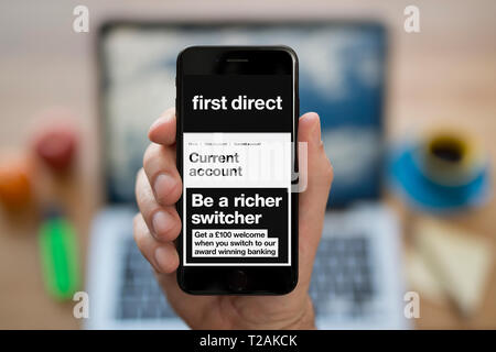 A man looks at his iPhone which displays the First Direct logo (Editorial use only). Stock Photo
