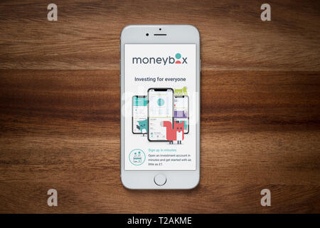 An iPhone showing the Moneybox website rests on a plain wooden table (Editorial use only). Stock Photo