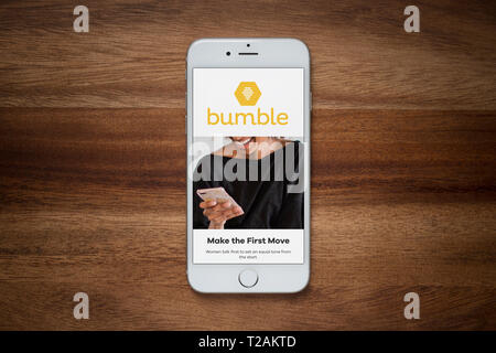 An iPhone showing the Bumble website rests on a plain wooden table (Editorial use only). Stock Photo