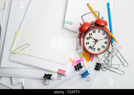 Alarm clock, over pile various documents, reports and receipt with colorful paperclip on white background. Deadline business and finance concepts Stock Photo