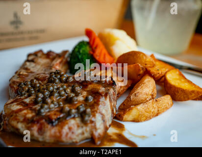 Selective focus on steak topped with sauce and pepper serve with potato fried and carrots, cauliflower and broccoli steamed. Steak on white plate Stock Photo