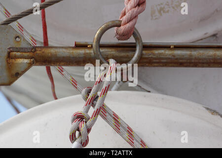 Steel rope and rusty hook on the back side of the sailing boat. Flag of Greece and historical castle on the background . Stock Photo
