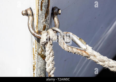 Steel rope and rusty hook on the back side of the sailing boat. Flag of Greece and historical castle on the background . Stock Photo