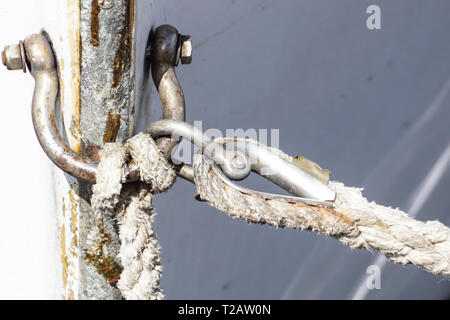 Steel rope and rusty hook on the back side of the sailing boat. Flag of Greece and historical castle on the background . Stock Photo