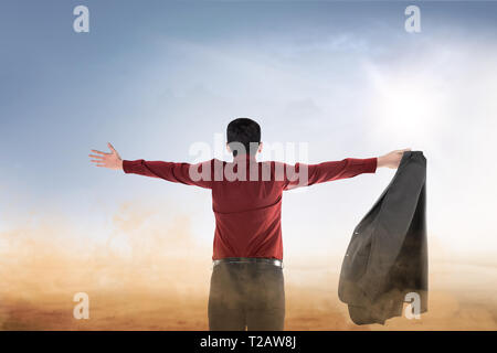 Rear view of asian businessman raised hands with open palm praying to god over blue sky background Stock Photo