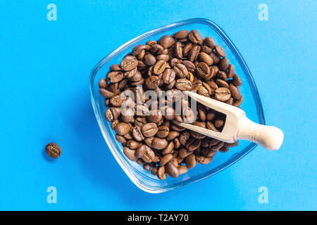Coffee beans in bowl with wood spoon over blue background Stock Photo