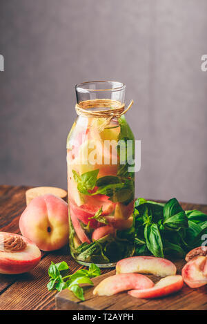 Bottle of Infused Water with Sliced Peach and Basil Leaves. Knife and Ingredients on Cutting Board. Vertical Orientation. Stock Photo