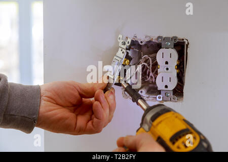 The hands of an electrician installing a power switch to the electrical junction box Stock Photo
