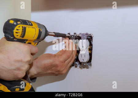 Electrician installs lighting switch in the wall using screwdriver Stock Photo